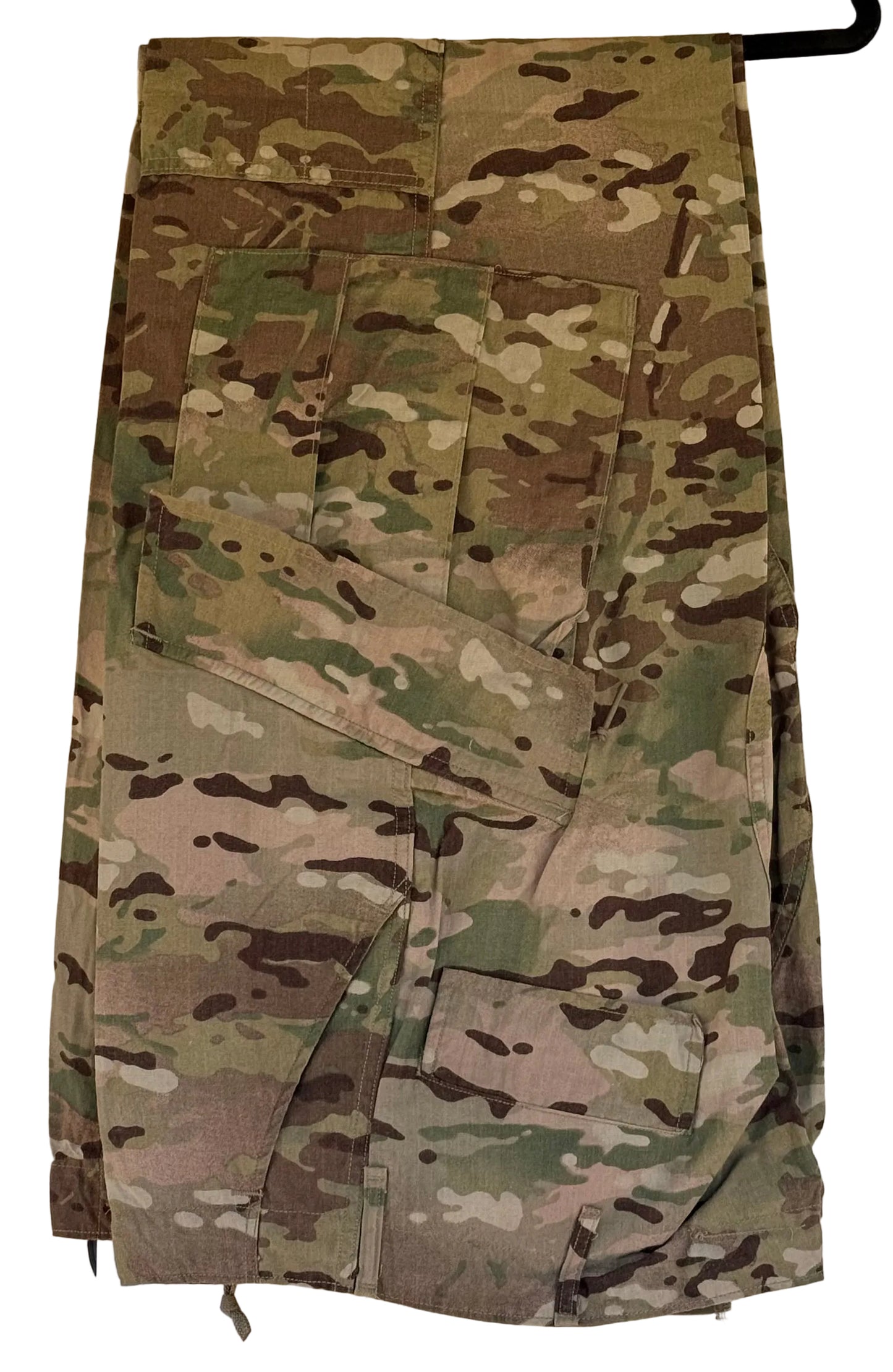 A pair of military cargo pants in a MultiCam camouflage pattern, hanging on a black hanger against a beige wall.