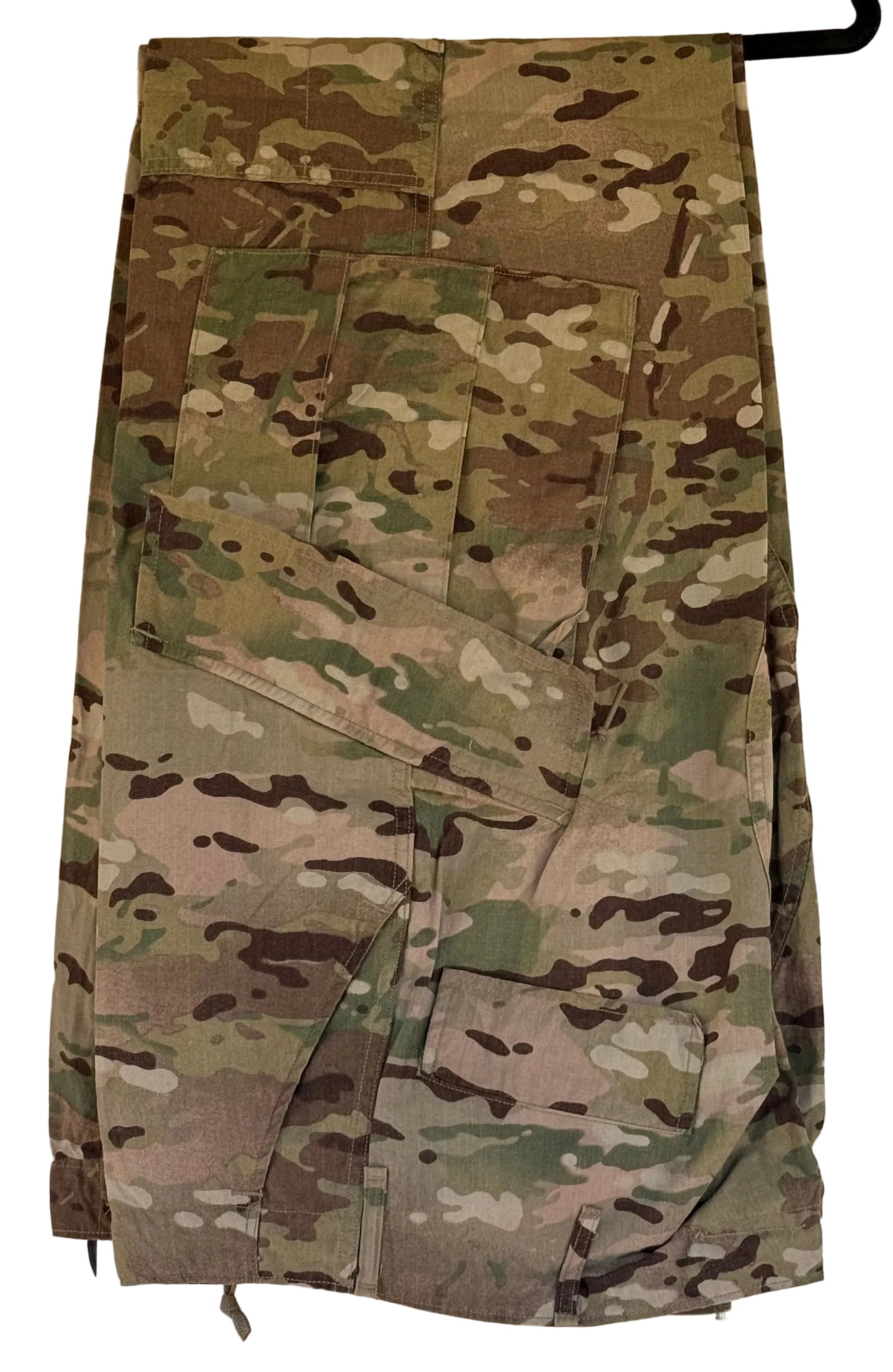 A pair of military cargo pants in a MultiCam camouflage pattern, hanging on a black hanger against a beige wall.