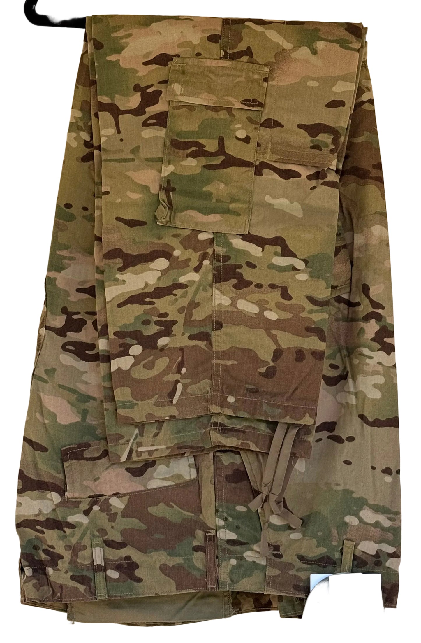 A pair of military cargo pants in MultiCam camouflage pattern, hanging on a black hanger against a beige wall. A white and black retail tag is visible in the bottom right corner.
