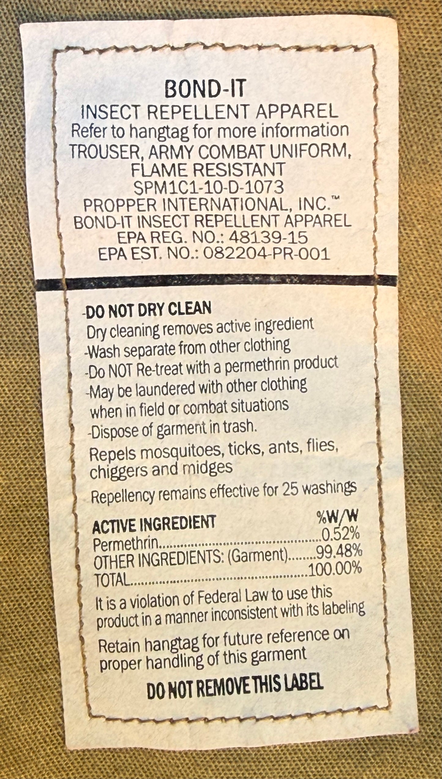A close-up of a white paper hangtag printed with product information for Bond-It Insect Repellent Apparel, placed on a tan textured fabric background.