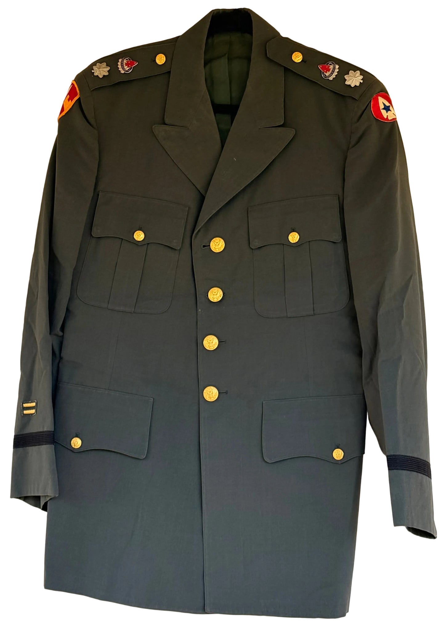 A dark olive green military uniform jacket with gold buttons, displayed flat against a plain beige wall. The jacket features shoulder epaulets with insignia, four front flap pockets, and sleeve tabs with rank stripes.