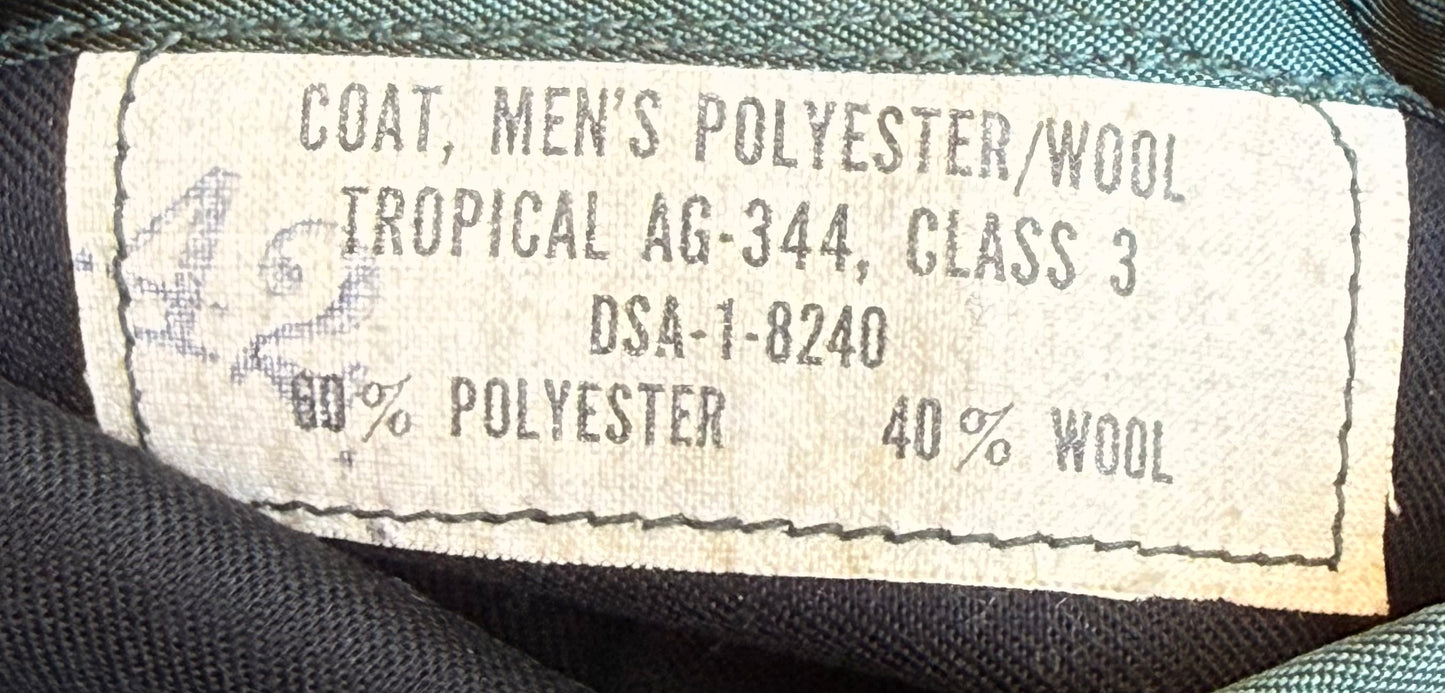 Close-up of a sewn-in fabric label reading 'COAT, MEN'S POLYESTER/WOOL TROPICAL AG-344, CLASS 3 DSA-1-8240 60% POLYESTER 40% WOOL' on dark navy woven fabric.