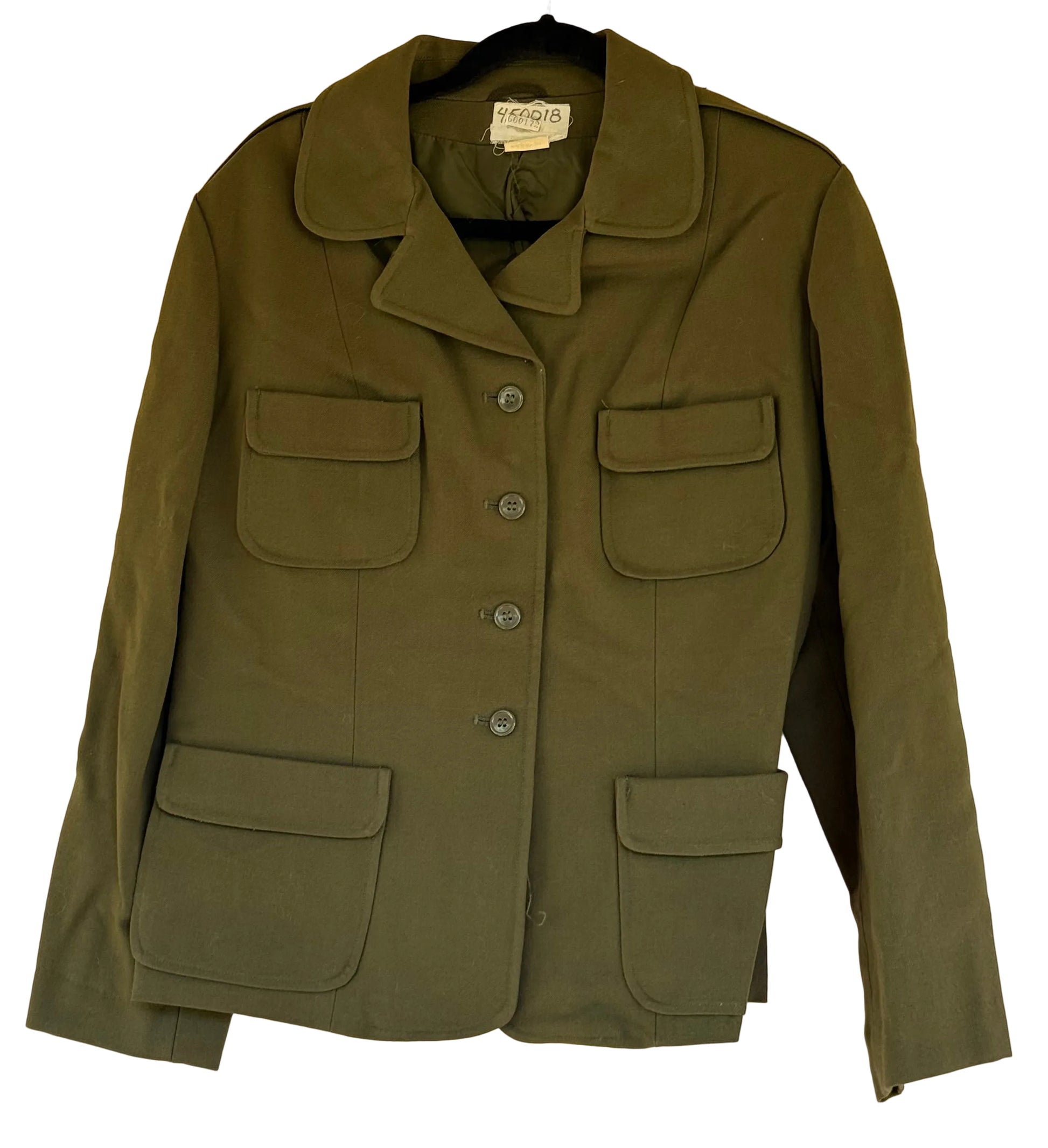 An olive green military-style utility jacket with four front flap pockets and a button front, hanging on a black hanger against a beige wall.
