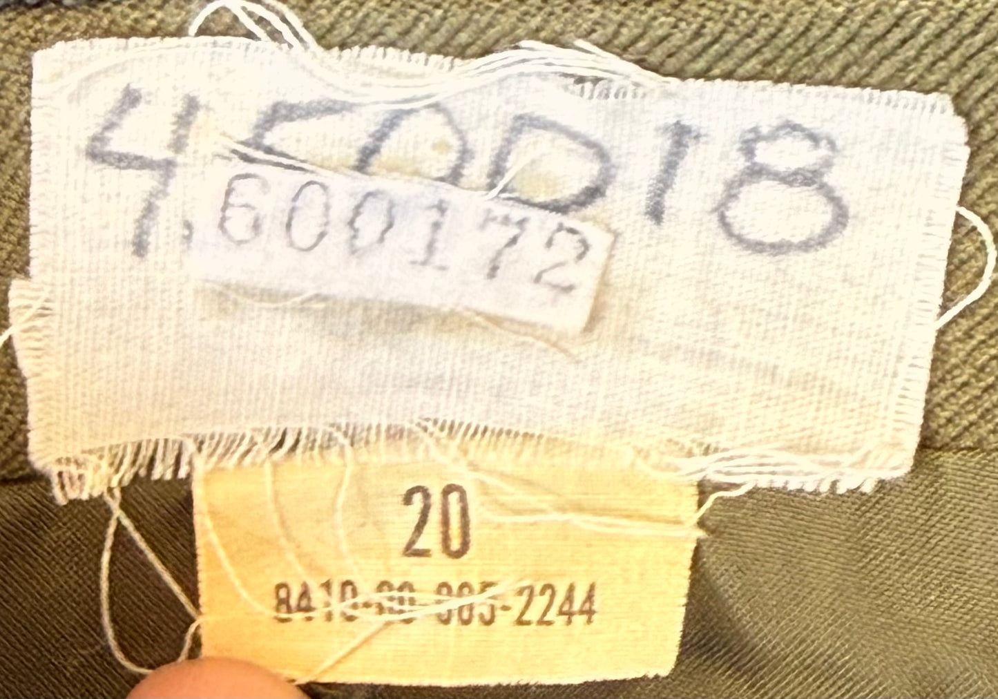 Close-up of a garment's interior label area showing a white woven fabric tag with dark printed numbers, a smaller white sticker overlay, and a yellow size tag reading 20.