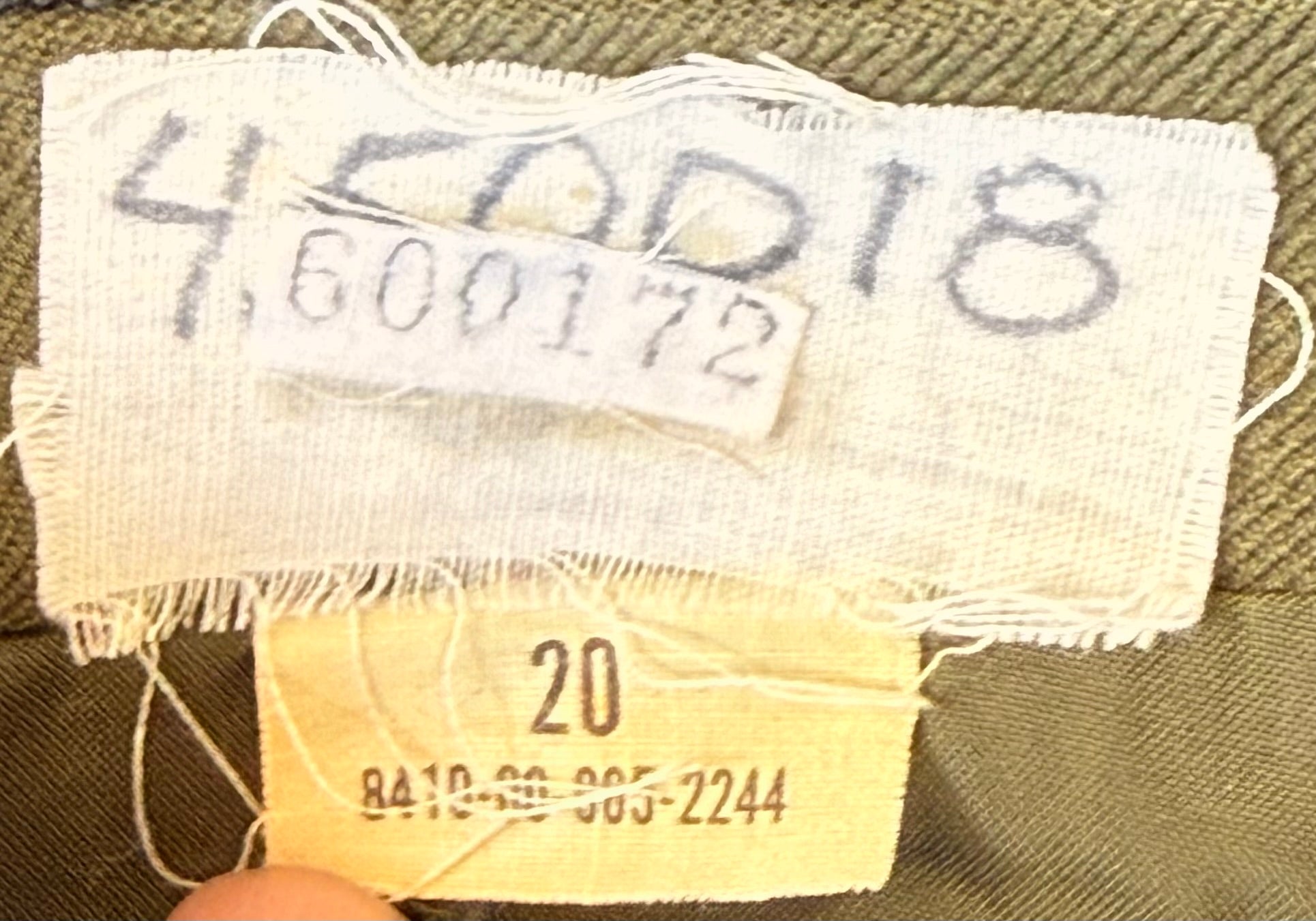 Close-up of a garment's interior label area showing a white woven fabric tag with dark printed numbers, a smaller white sticker overlay, and a yellow size tag reading 20.
