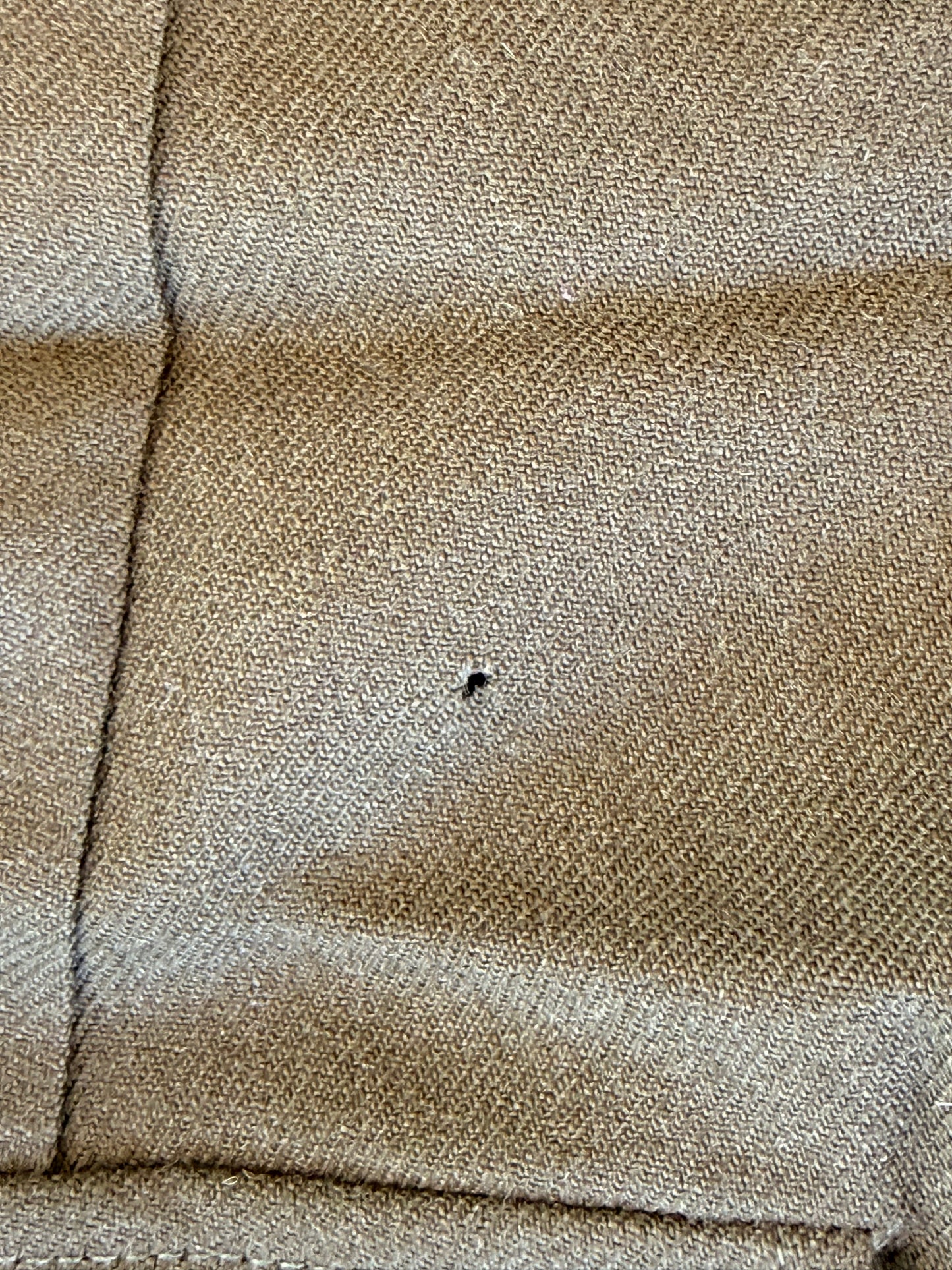Close-up of a beige woven fabric with visible texture, a vertical seam, and a small dark speck or hole near the center.