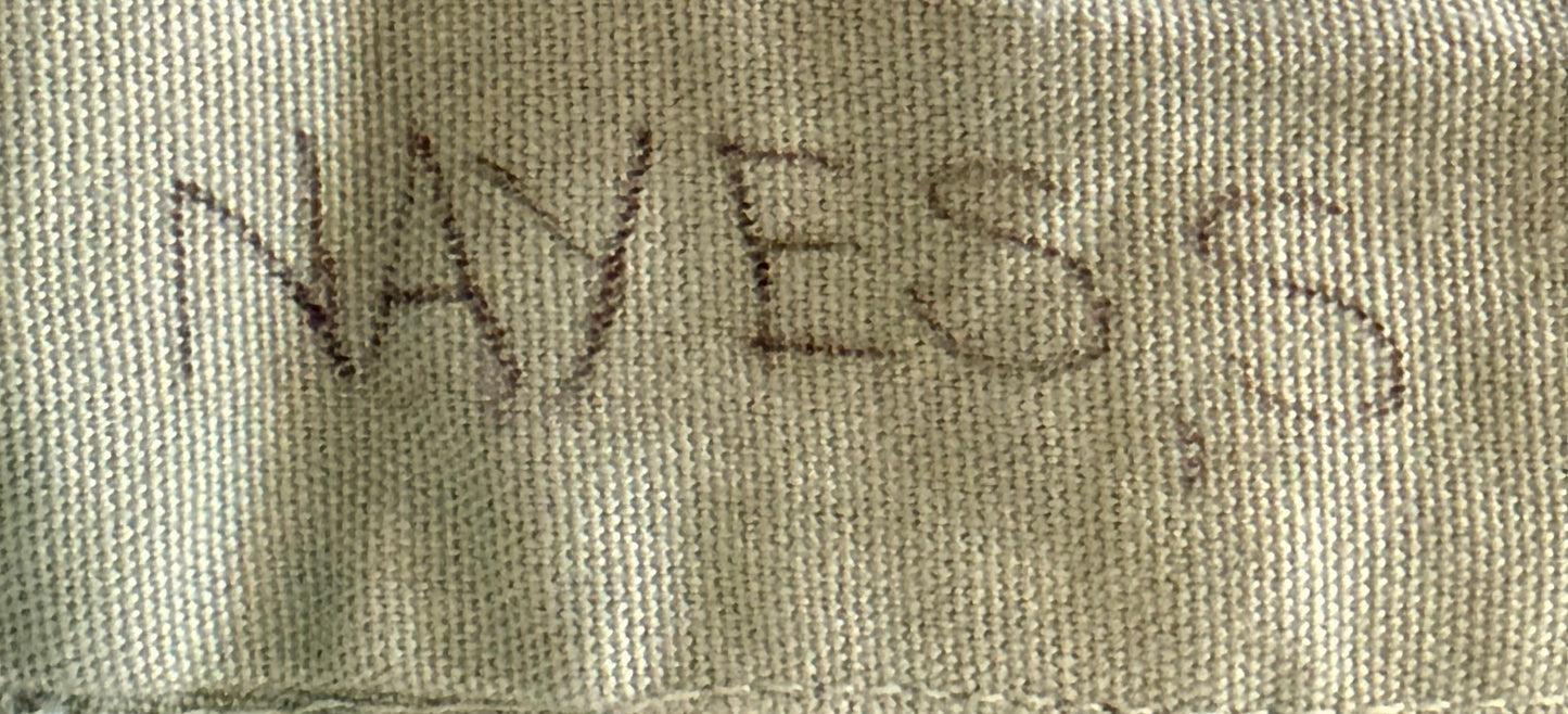 A close-up of a beige woven fabric with the word 'NAYES' written in dark brown or black marker, with a comma after the final letter.