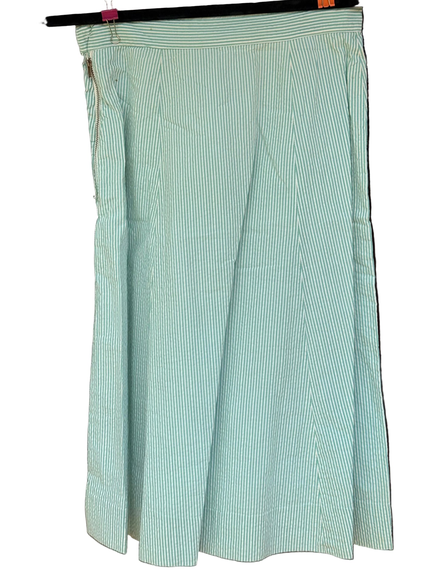 A light green and white vertically striped midi skirt hanging from a black hanger against a dark wooden background.