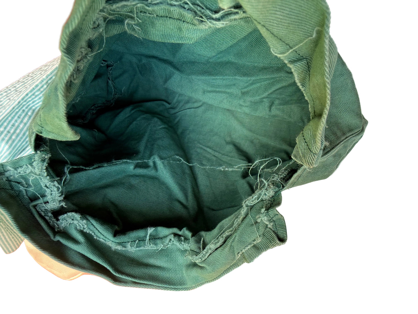 An open dark green canvas drawstring bag with frayed edges, photographed from inside looking out onto a striped fabric surface.