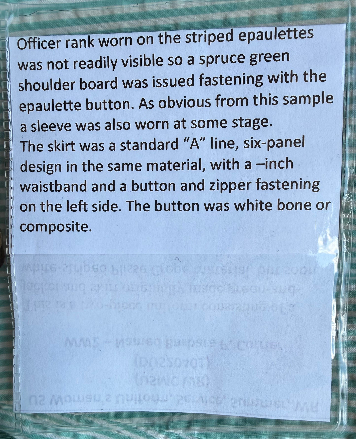 A printed instruction card explaining the fit and construction of officer rank epaulettes worn on striped green and white uniform jackets, sealed in a clear plastic sleeve and photographed on the fabric background.