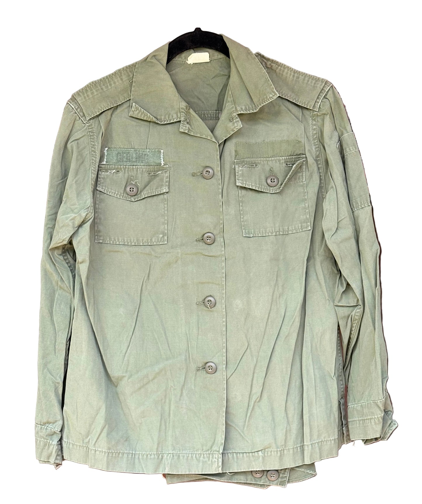An olive green military-style utility jacket hanging on a black hanger against a carved dark brown wooden door.