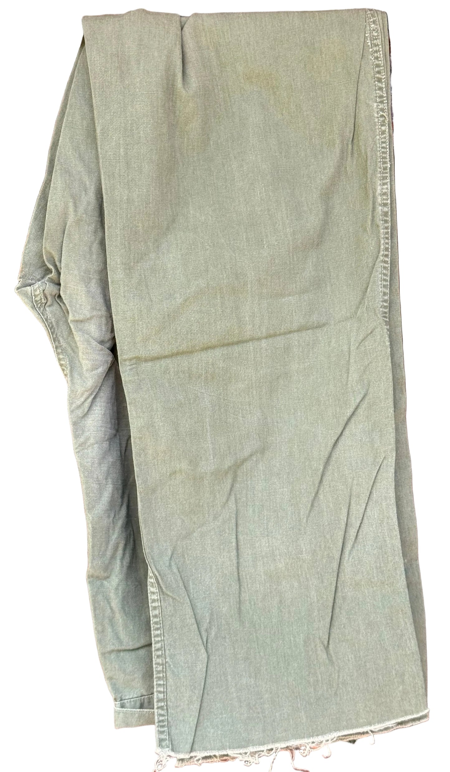 A pair of light olive green canvas pants hanging on a black hanger against a dark brown wooden background.