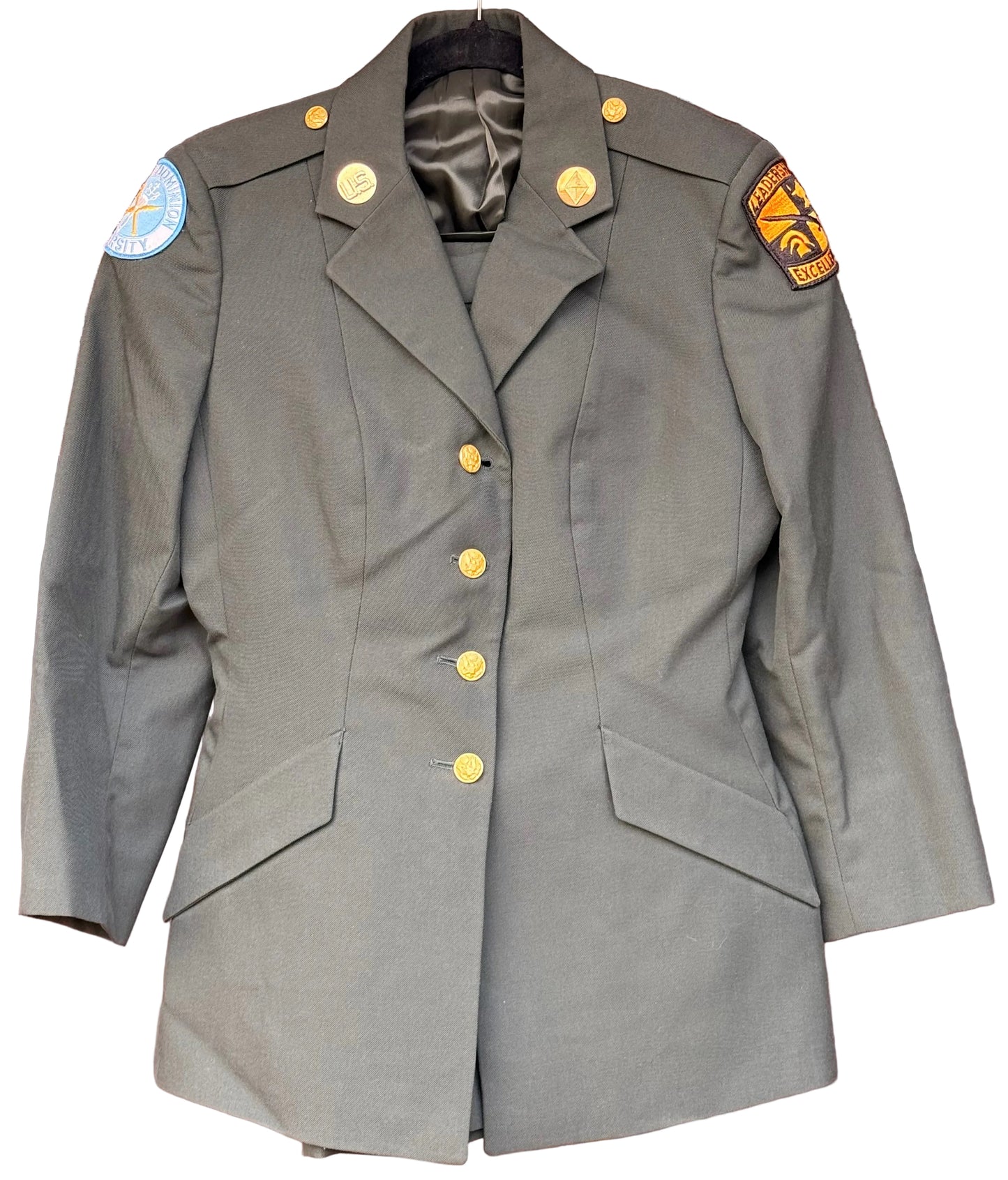 An olive drab military-style blazer jacket with gold buttons, displayed on a hanger against a carved wooden background. It features shoulder patches, one of which reads '101st Airborne Division'.