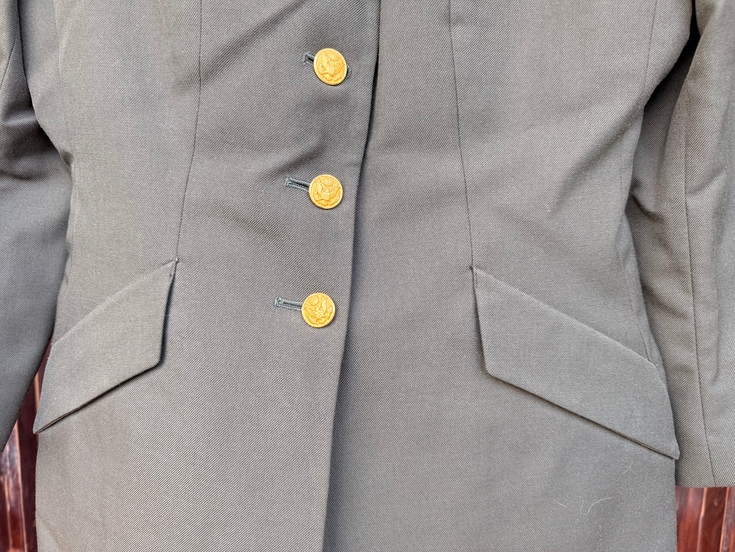 Close-up of a gray double-breasted jacket with three gold buttons and flap pockets.