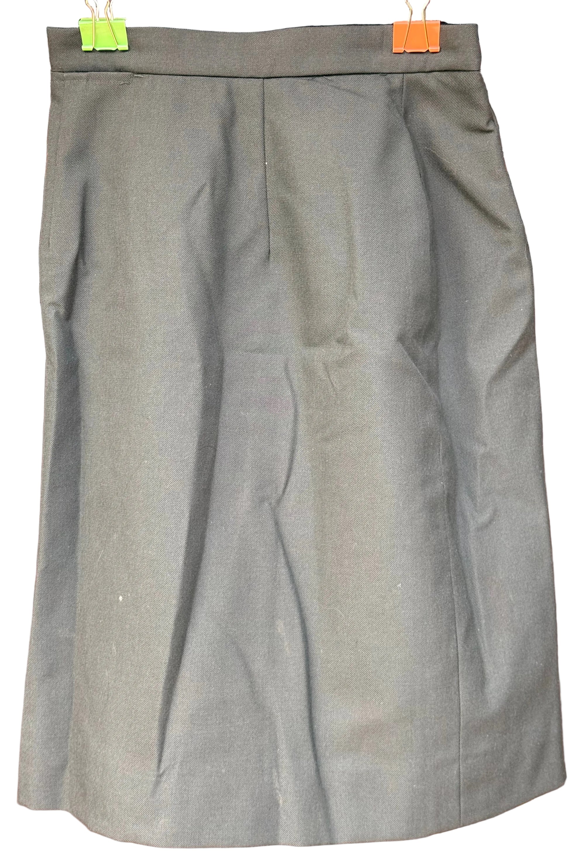 An olive green A-line skirt hanging from a black hanger with green and orange clips, set against a dark wood background.