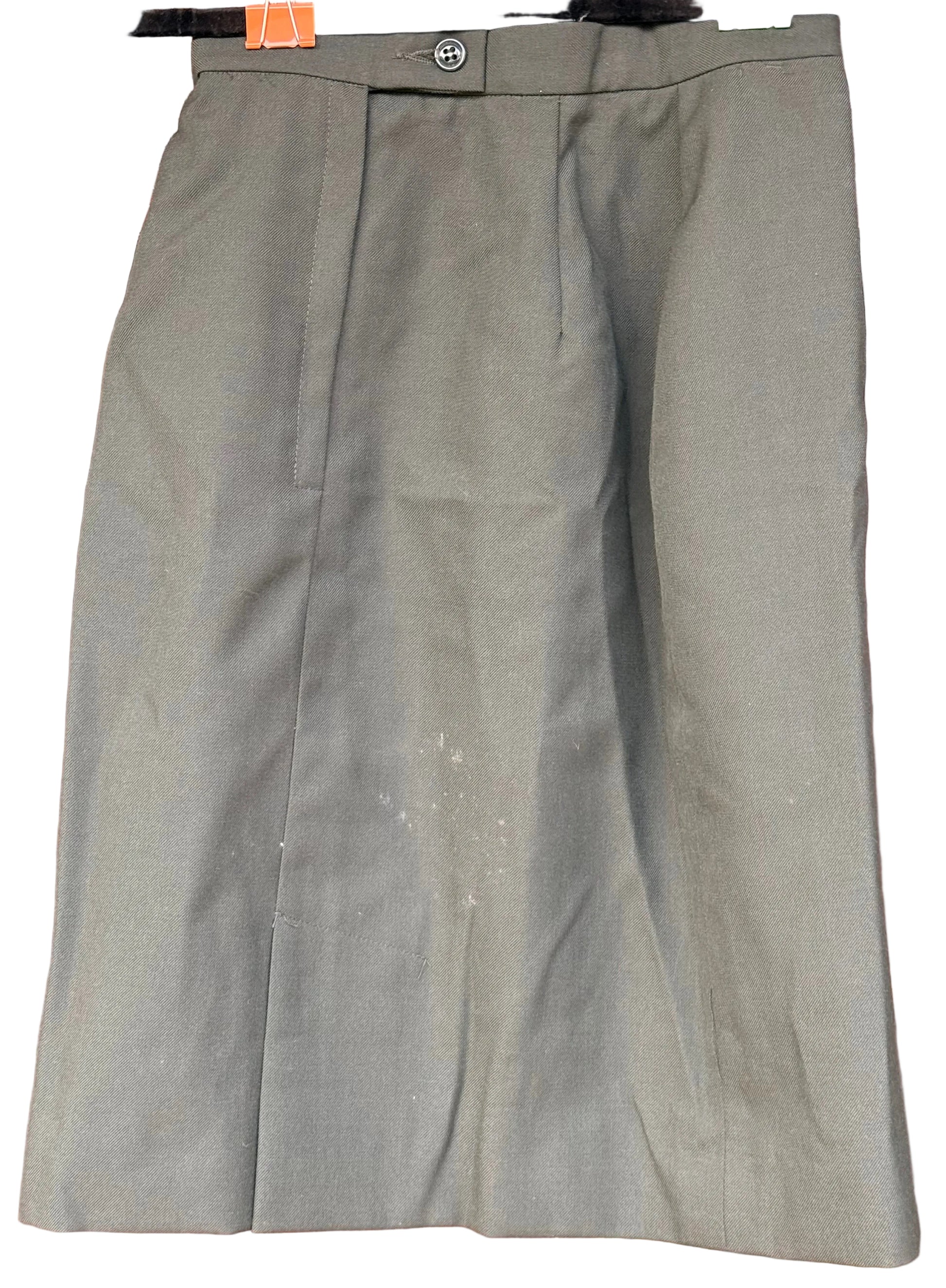An olive green pleated skirt hanging on a black hanger against a carved wooden background.