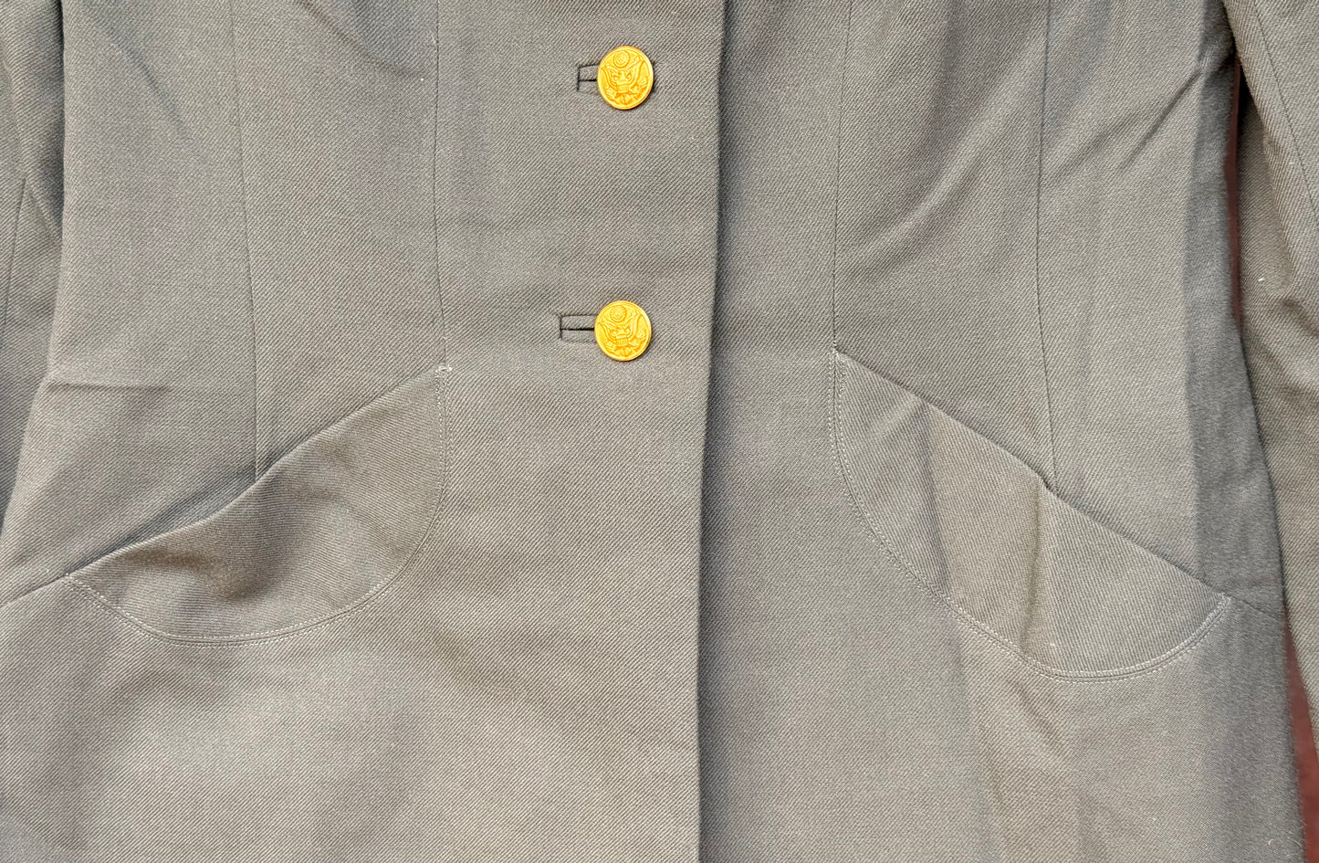 Close-up of a gray jacket or coat with two round gold buttons and angled front pockets.