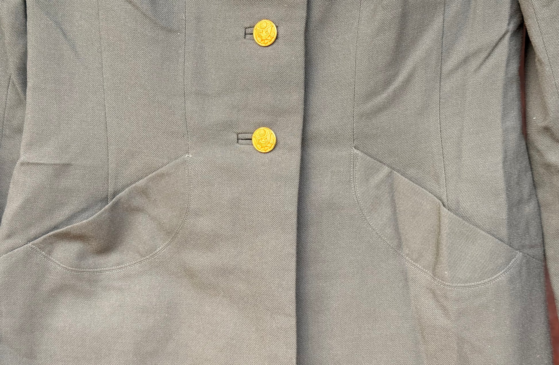 Close-up of a gray jacket or coat with two round gold buttons and angled front pockets.