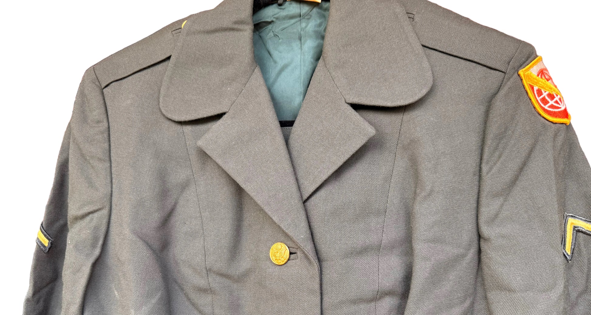 A military-style olive drab double-breasted jacket with gold buttons, displayed on a hanger against a carved wooden background.