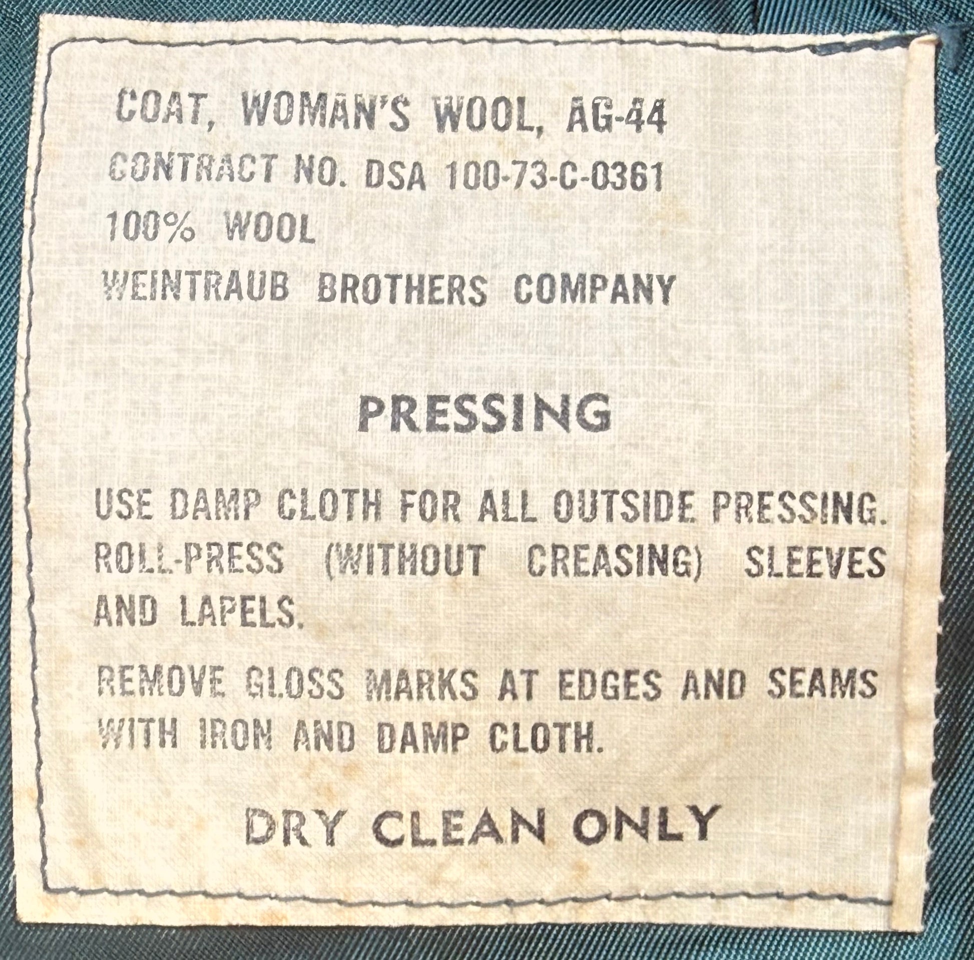 A close-up of a vintage wool garment label reading 'COAT, WOMAN'S WOOL, AG-44' and 'PRESSING' with care instructions, sewn onto dark teal fabric.