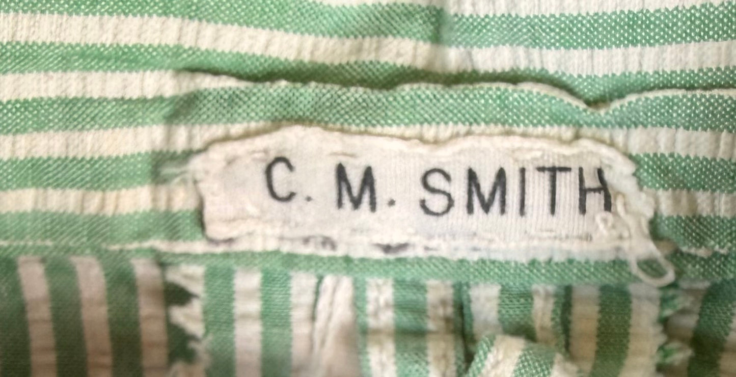 Close-up of a green and white striped fabric garment with a sewn-on fabric label reading 'C. M. SMITH'.