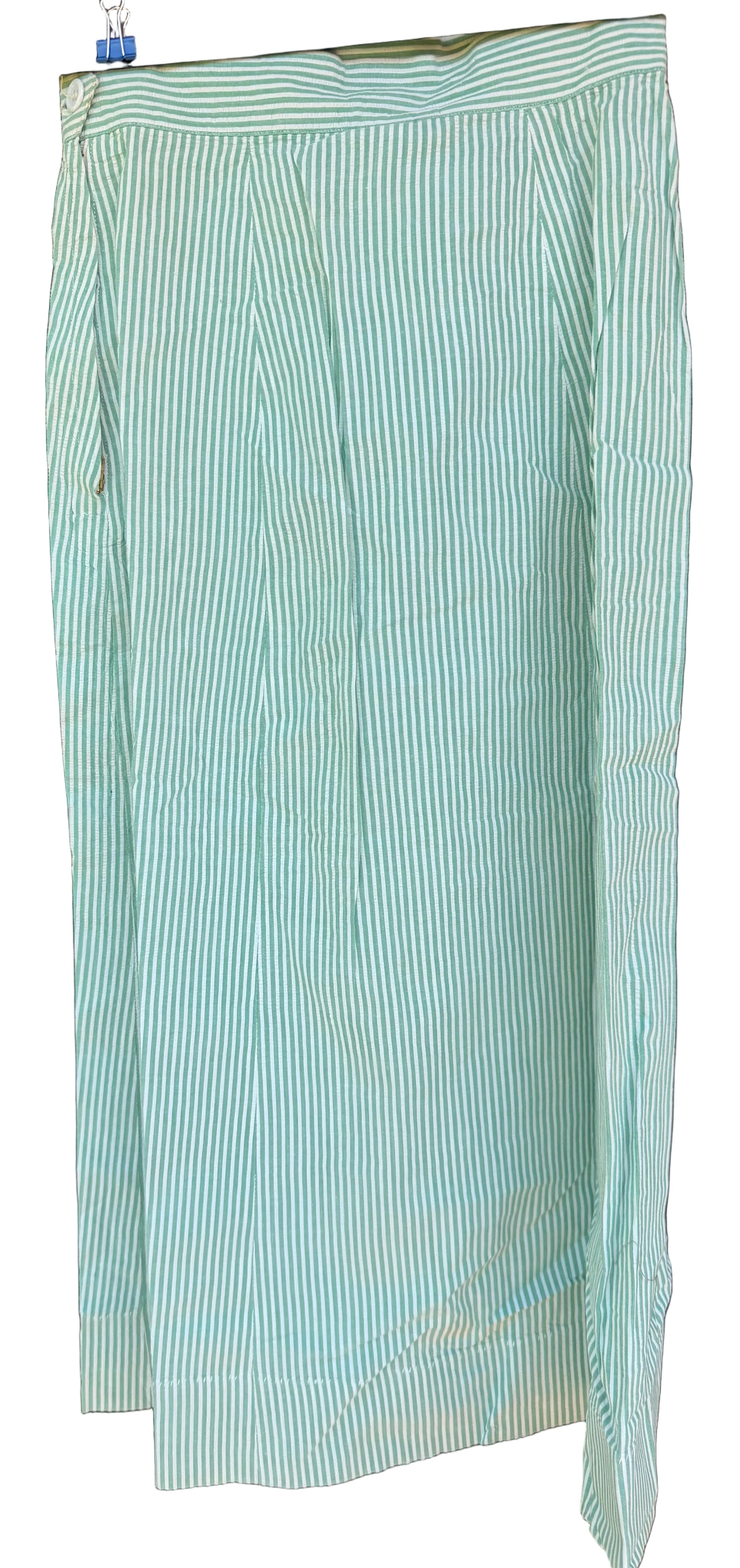 A light mint green and white vertically striped skirt hanging on a black hanger against a dark brown wooden background.