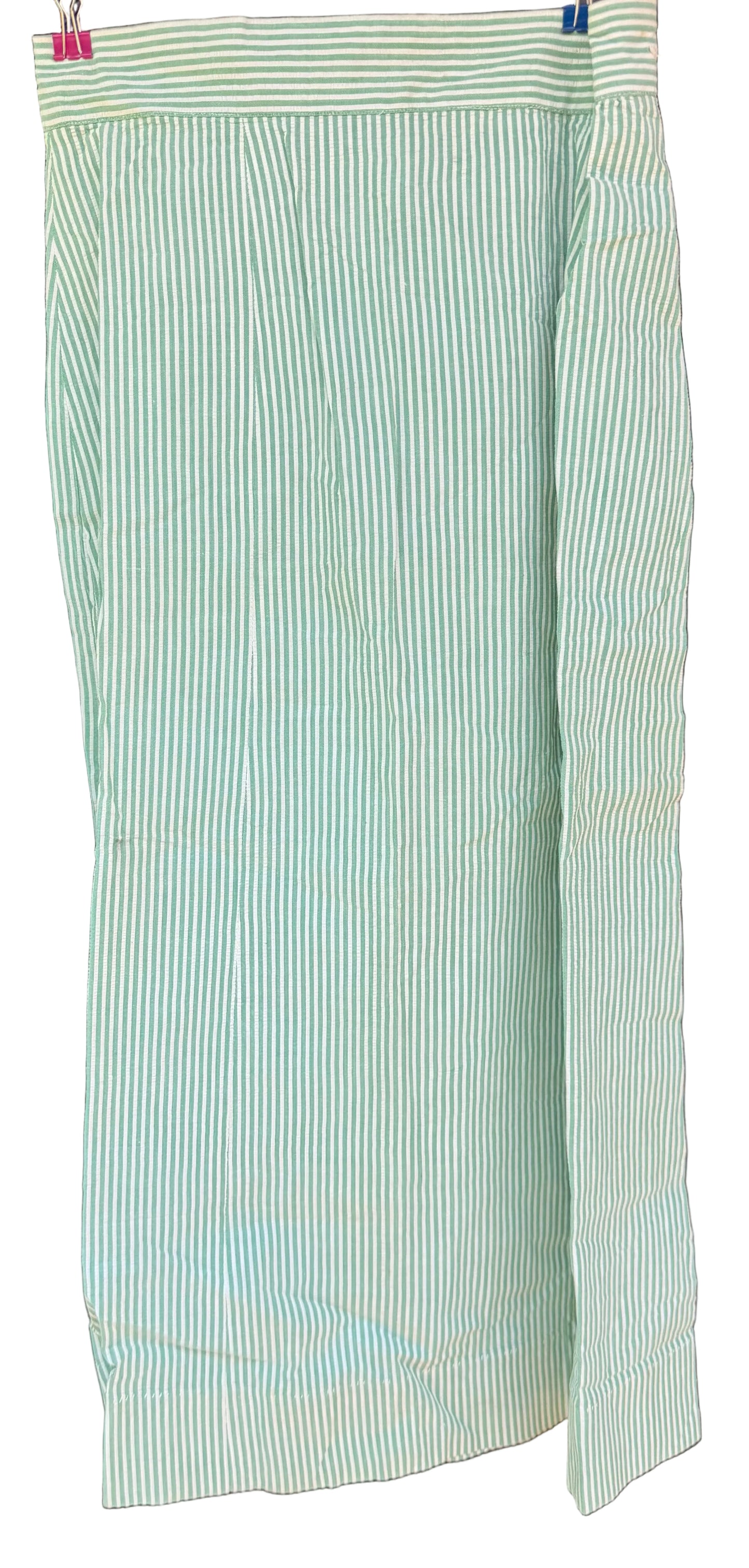 A light green and white vertically striped fabric garment, likely a skirt or drape, hanging against a dark wooden background.