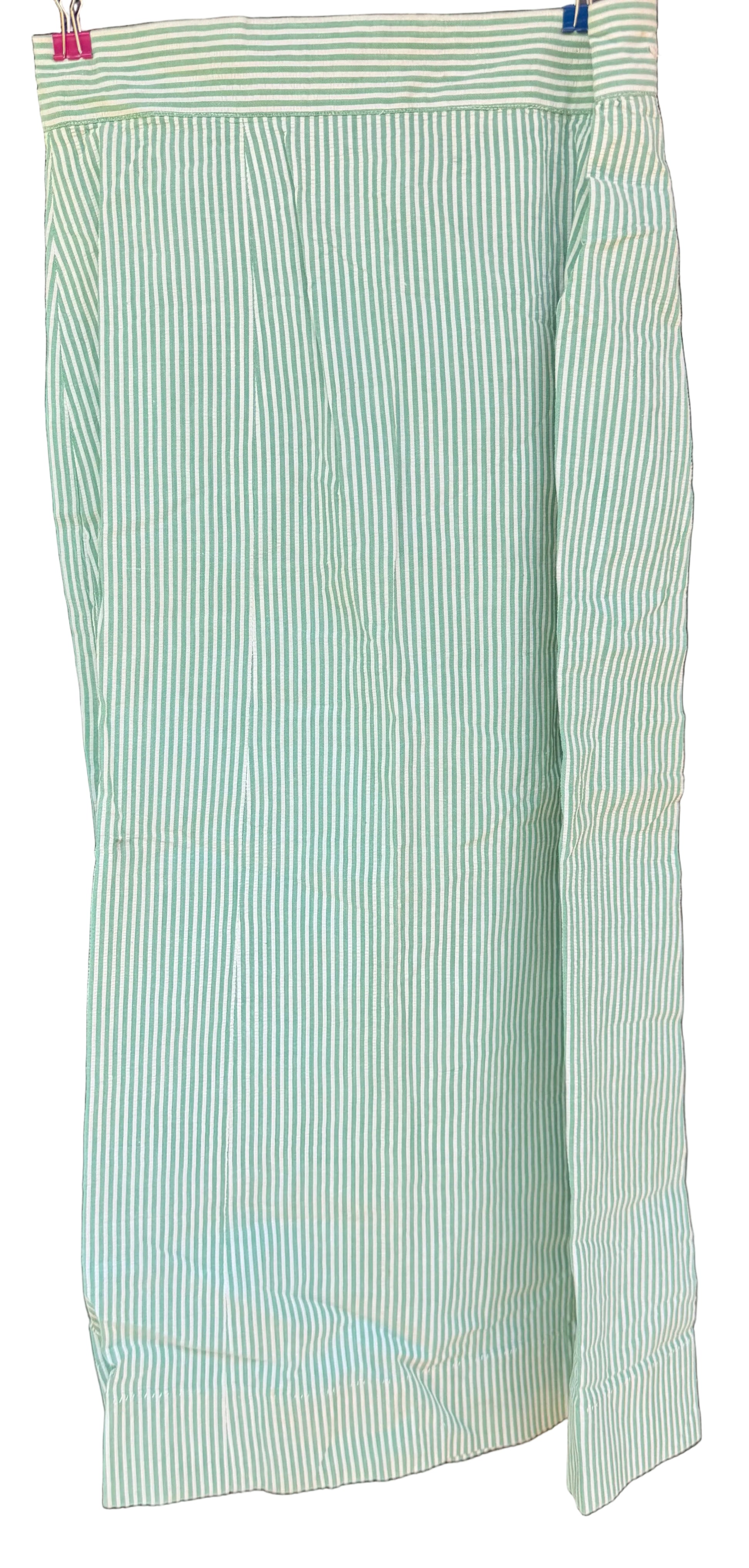 A light green and white vertically striped fabric garment, likely a skirt or drape, hanging against a dark wooden background.