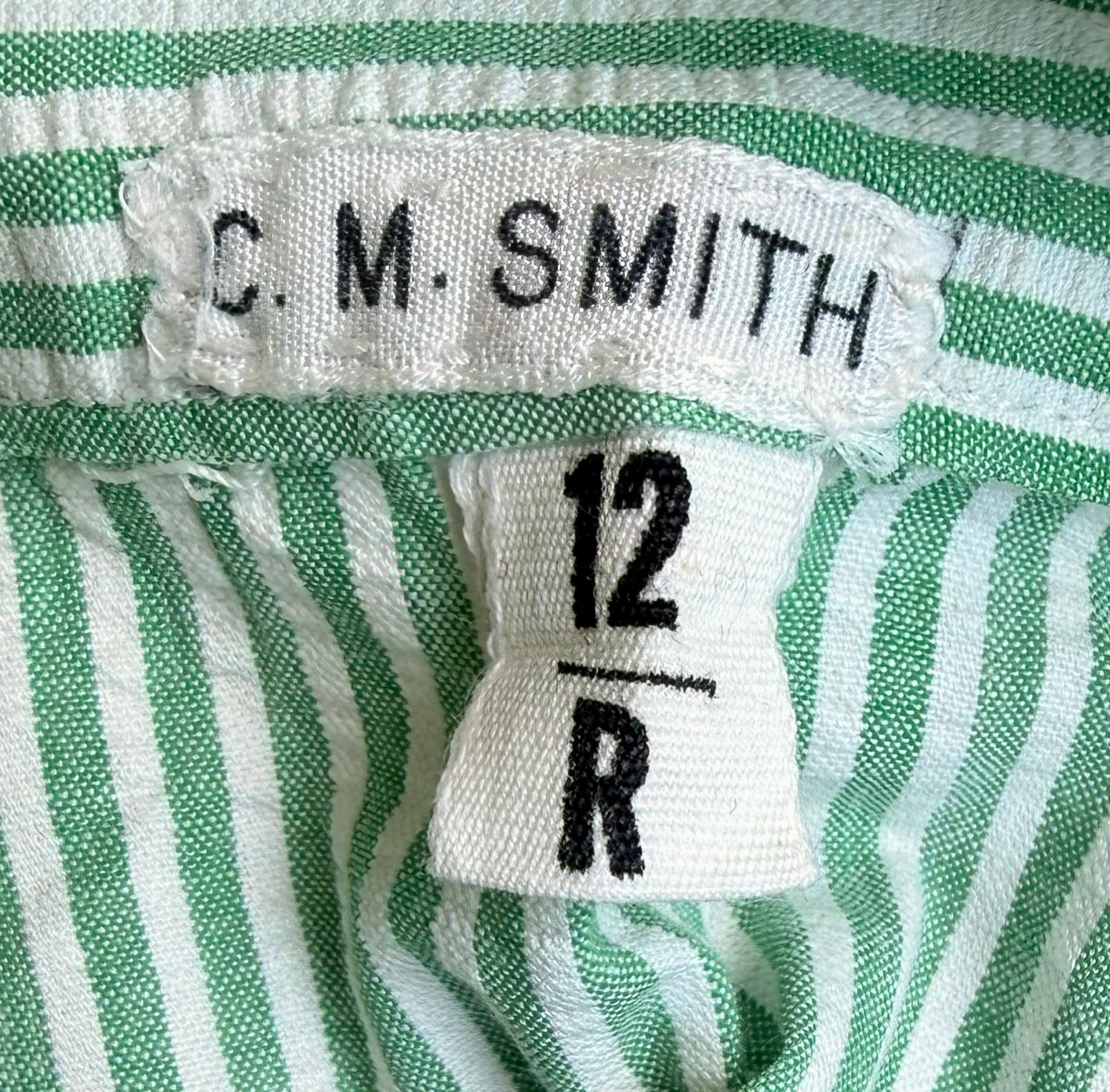 Close-up of a green and white striped garment showing a white woven brand label reading C. M.