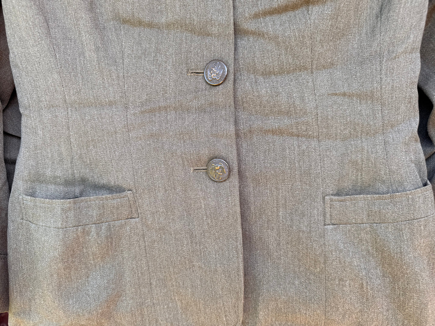 Close-up of a light beige textured blazer or jacket with two decorative buttons and side pockets, shown on a person wearing it.