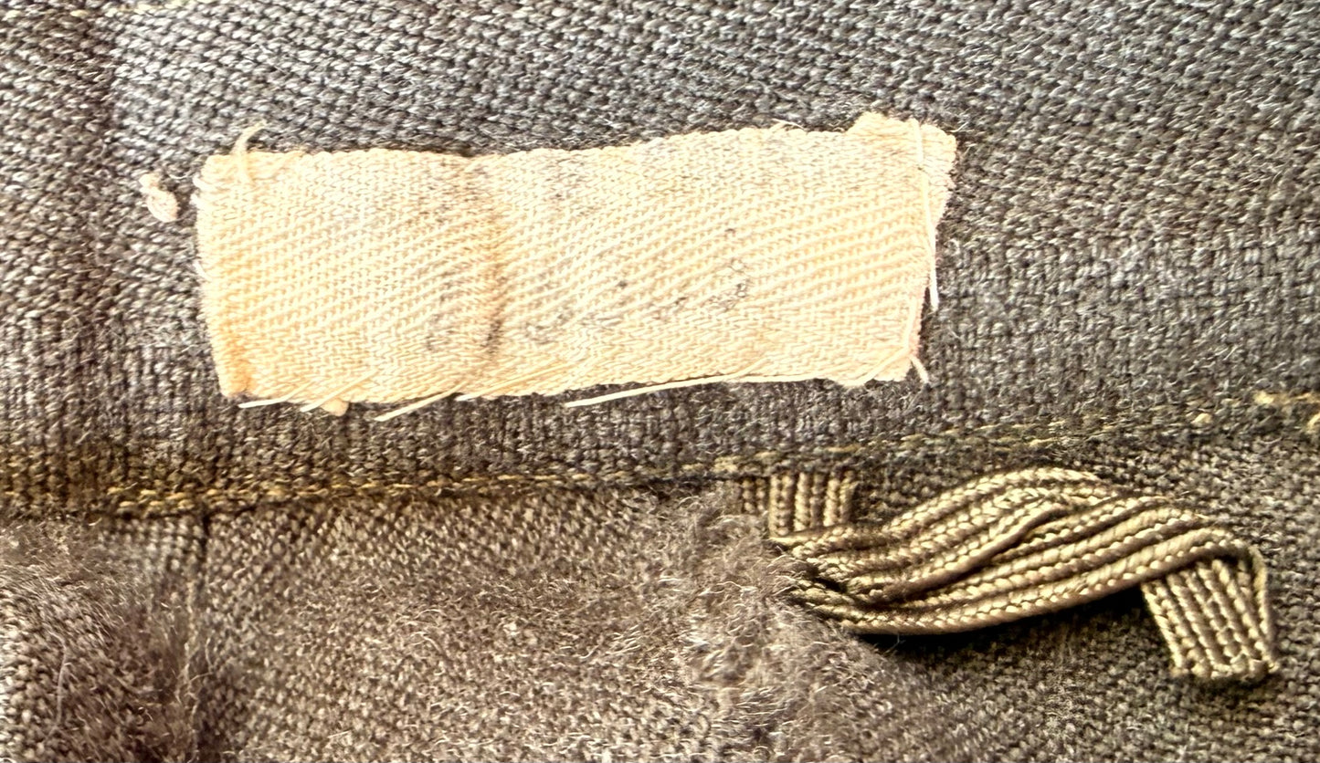 Close-up of a vintage brown woven textile, likely a jacket or coat, showing a light beige fabric label sewn onto the inside and a matching brown woven tie closure.